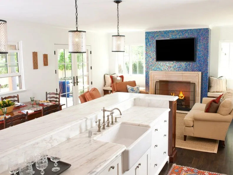 Tall blue-purple mosaic fireplace wall with television seen from pale open-plan kitchen and living area