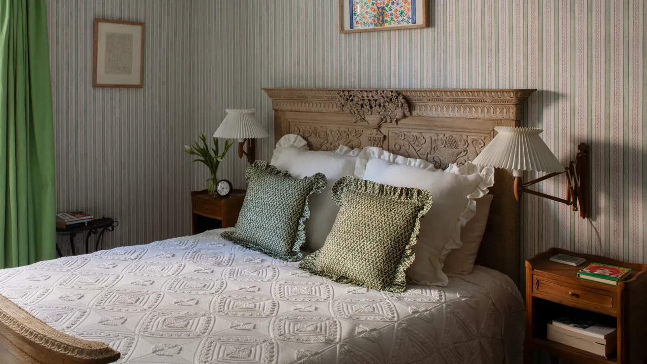 A tall characterful headboard stands behind pale bedding beside a timber nightstand.