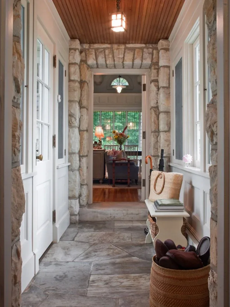Narrow stone entrance with white glazed door, white bench, basket, wood ceiling and windows beside the route