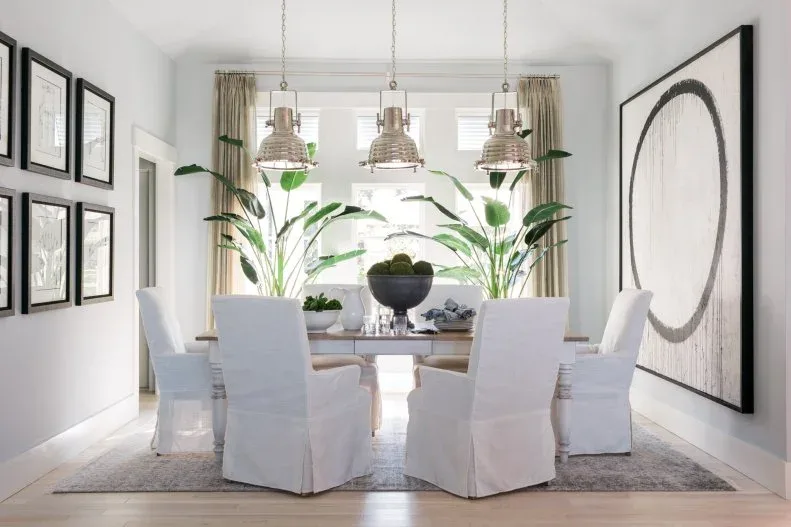Small dark-framed picture grid opposite a large circular artwork beside a round dining table and white chairs