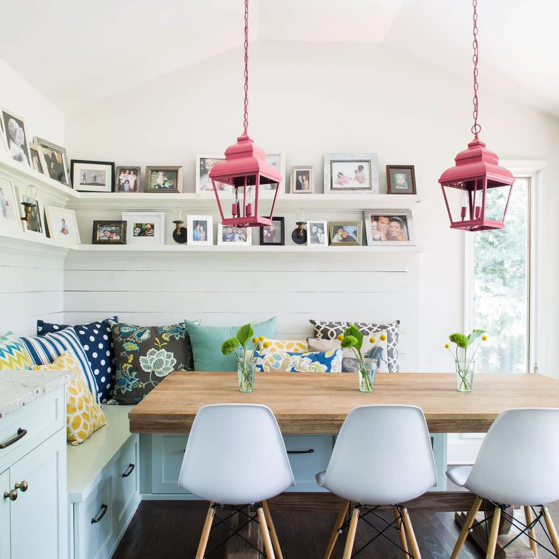 White corner picture shelves above a colorful dining bench with white chairs and two pink lantern lights