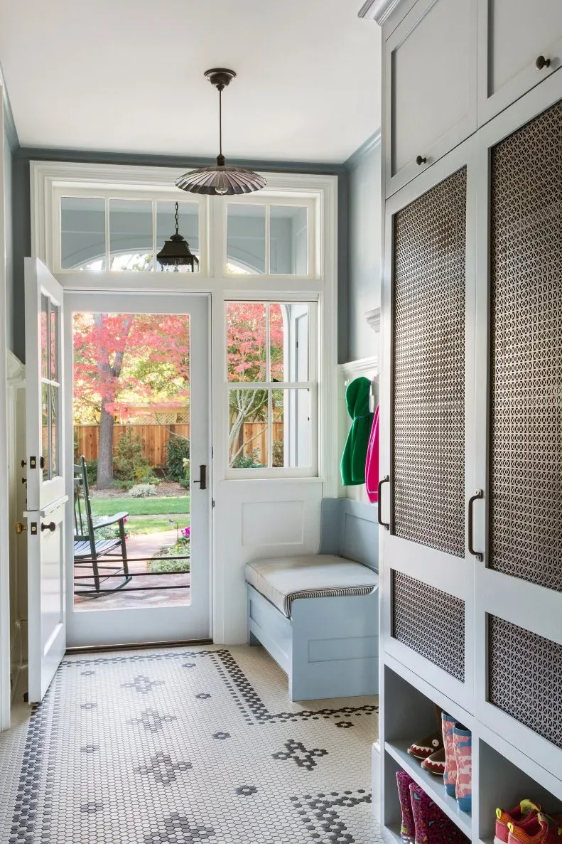 Pale blue mudroom with tall textured-panel cupboard, small bench nook, patterned floor and glazed exterior door.