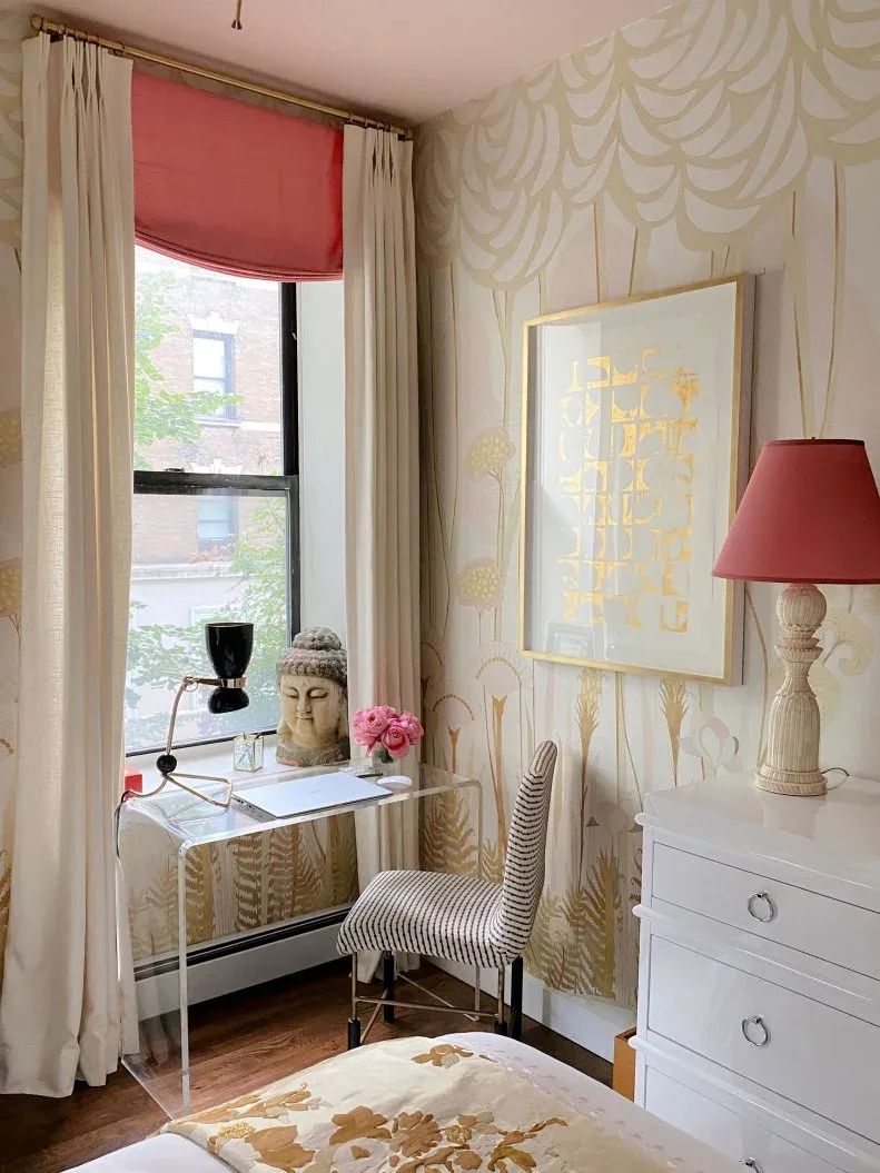 Clear desk with a striped chair beside a bedroom window, gold-toned patterned wallpaper and a coral blind.