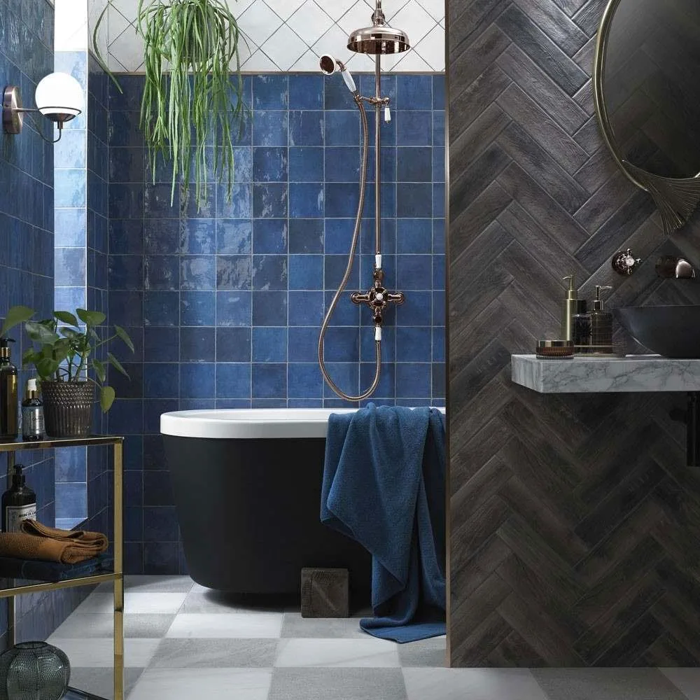 Deep blue square tiles surround a black bath beside a dark herringbone-patterned partition