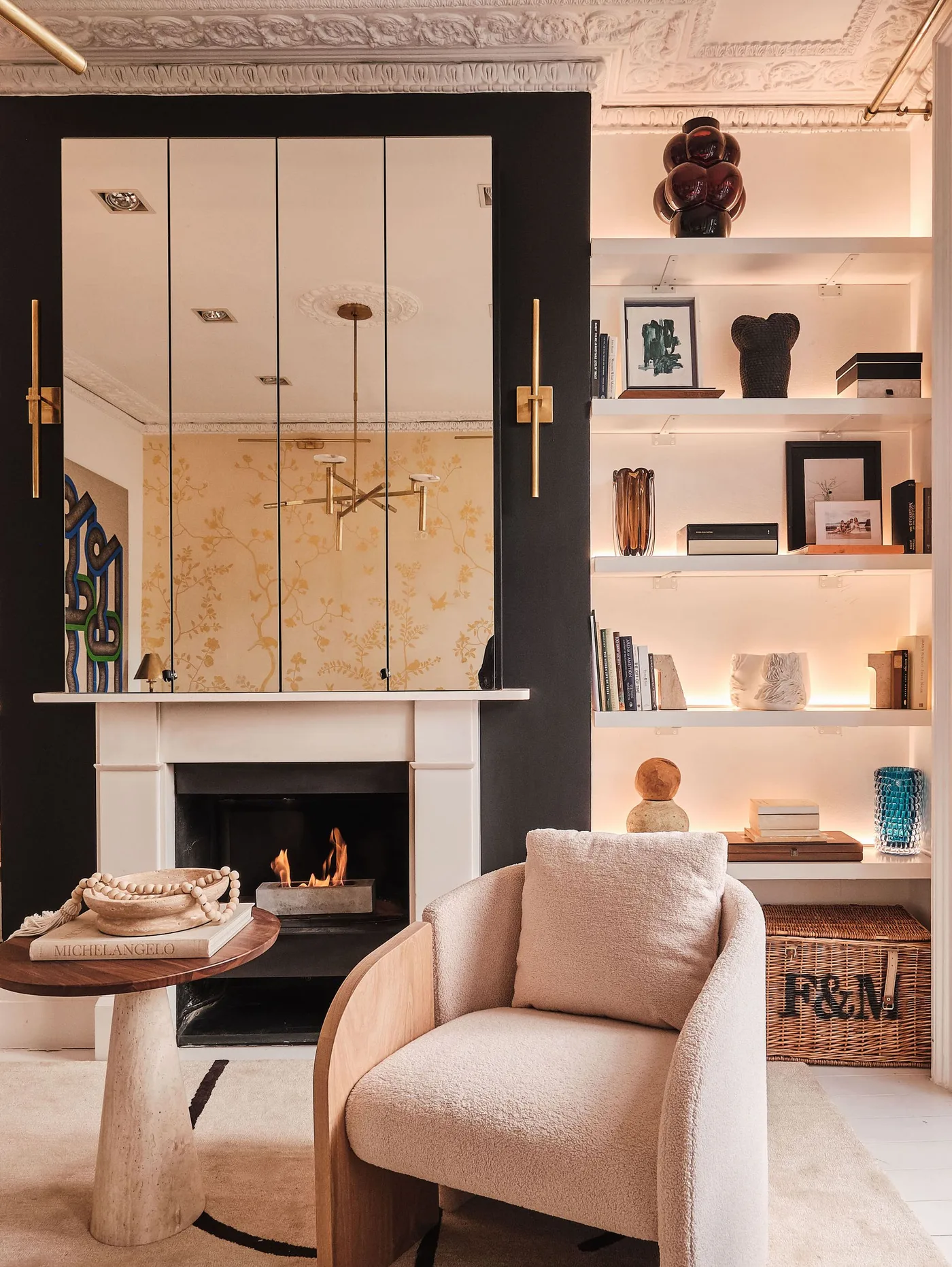 Illuminated pale alcove shelves beside dark fireplace breast with tall divided mirror and pale chair
