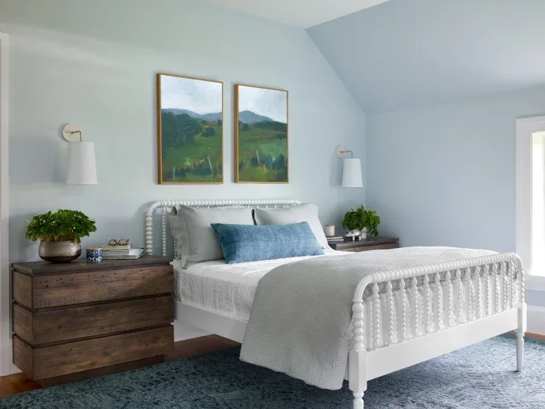 Pale blue bedroom with white spindle bed, wood bedside drawers and two landscape pictures