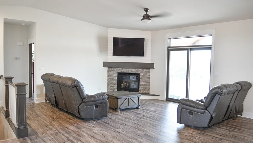 Corner fireplace beneath a television with two gray reclining chairs and a small central table.