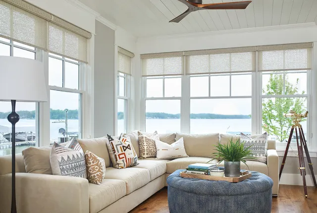 A pale sofa faces broad windows beside a large blue upholstered ottoman.