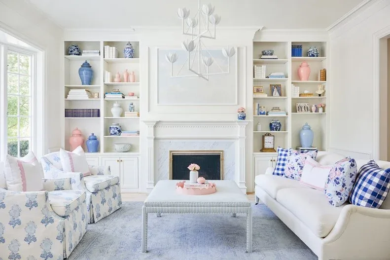 White traditional fireplace between pale shelves of blue and pink vessels, with floral chair and checked cushions