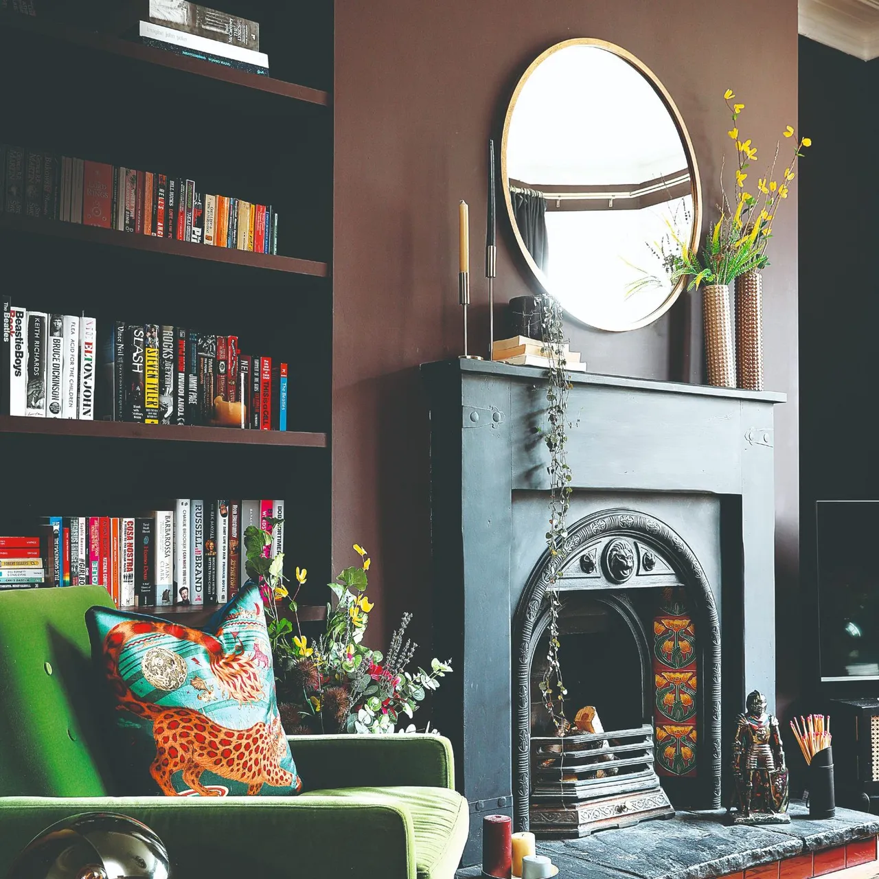 Gray fireplace mantel with two slender unlit candles beside a round mirror and tall flower vase.