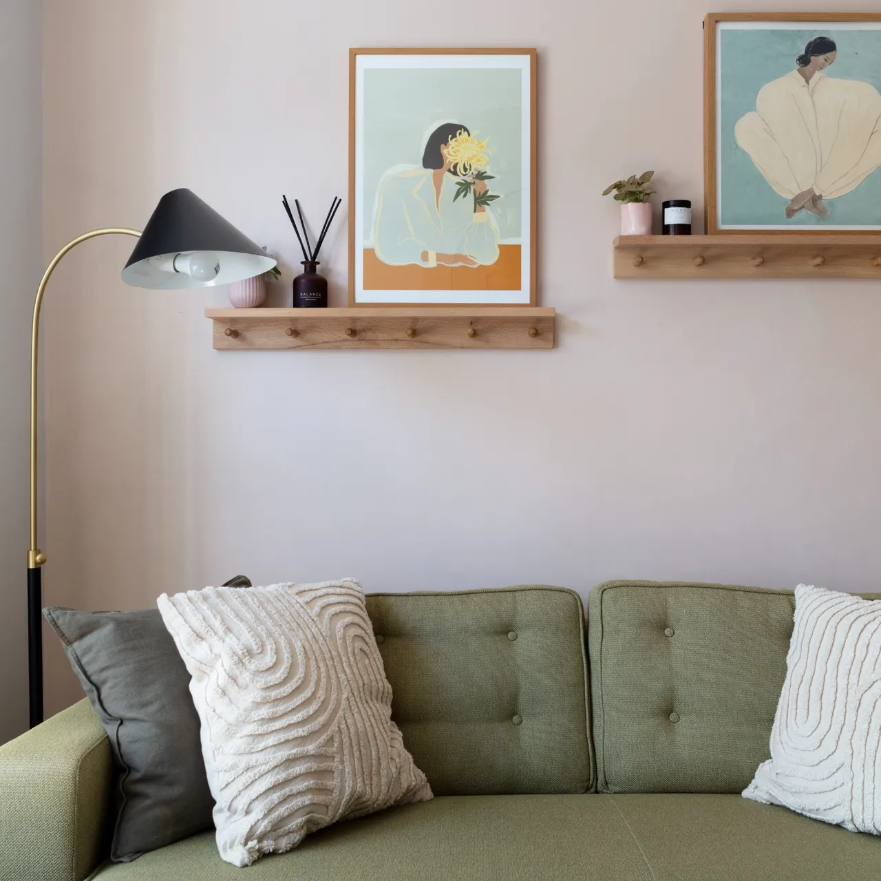 A compact green sofa sits beneath two small timber shelves and framed pictures