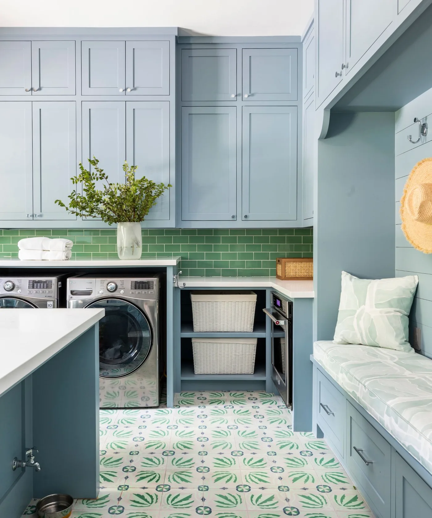 Blue laundry cupboards and island with green rectangular backsplash, patterned floor, open basket shelves and a cushioned seat