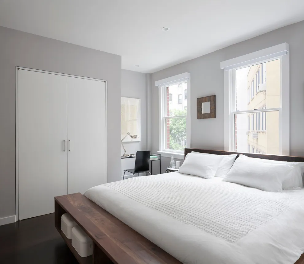 A pale bed sits close to built-in storage above a dark wood floor