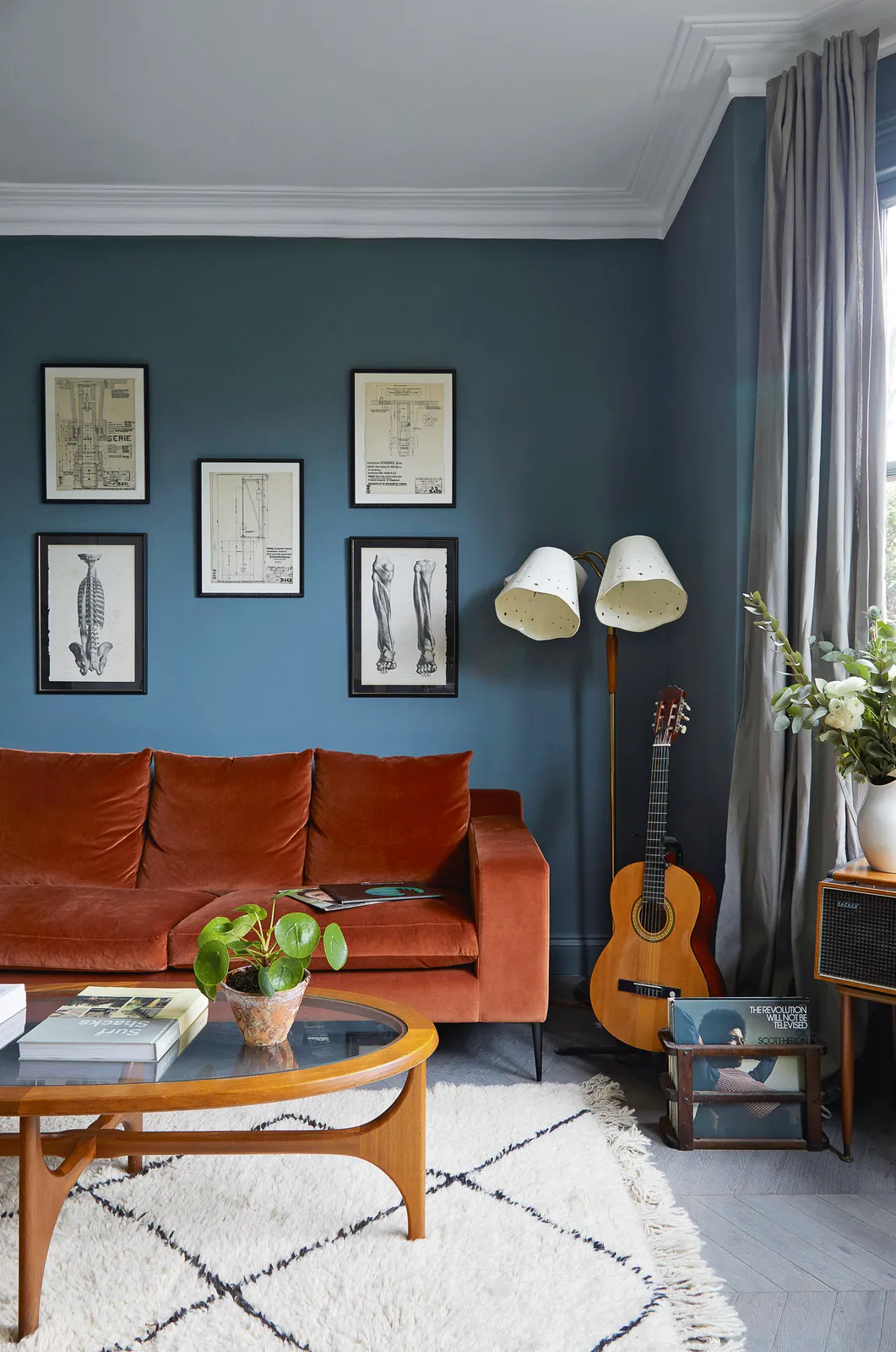 Muted blue walls sit behind a rust-colored sofa and framed pictures.