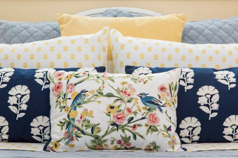 Close view of pale blue quilt, yellow cushions, navy patterned pillows and small floral cushion