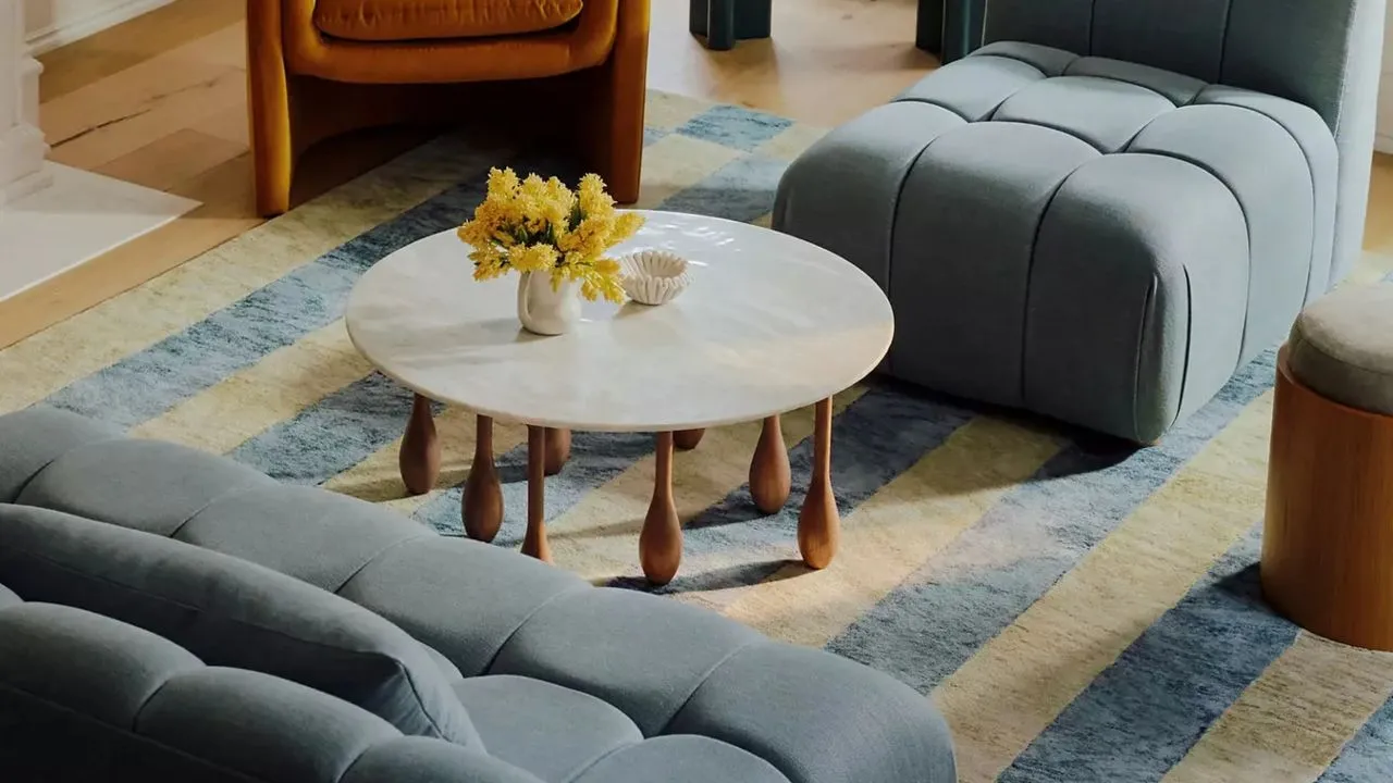 Soft blue seating sits around a pale table on a lightly striped rug.