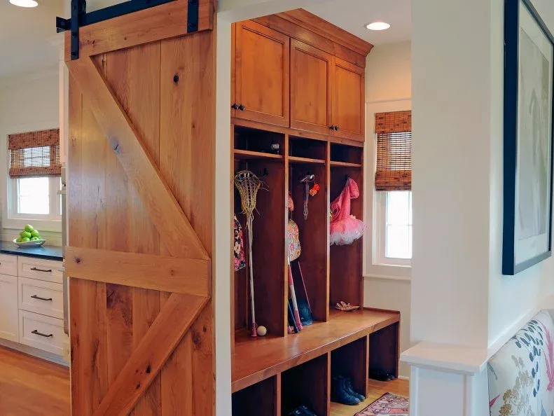 Wood mudroom cupboards and individual hanging bays with bench beside a sliding barn-style door and pale walls