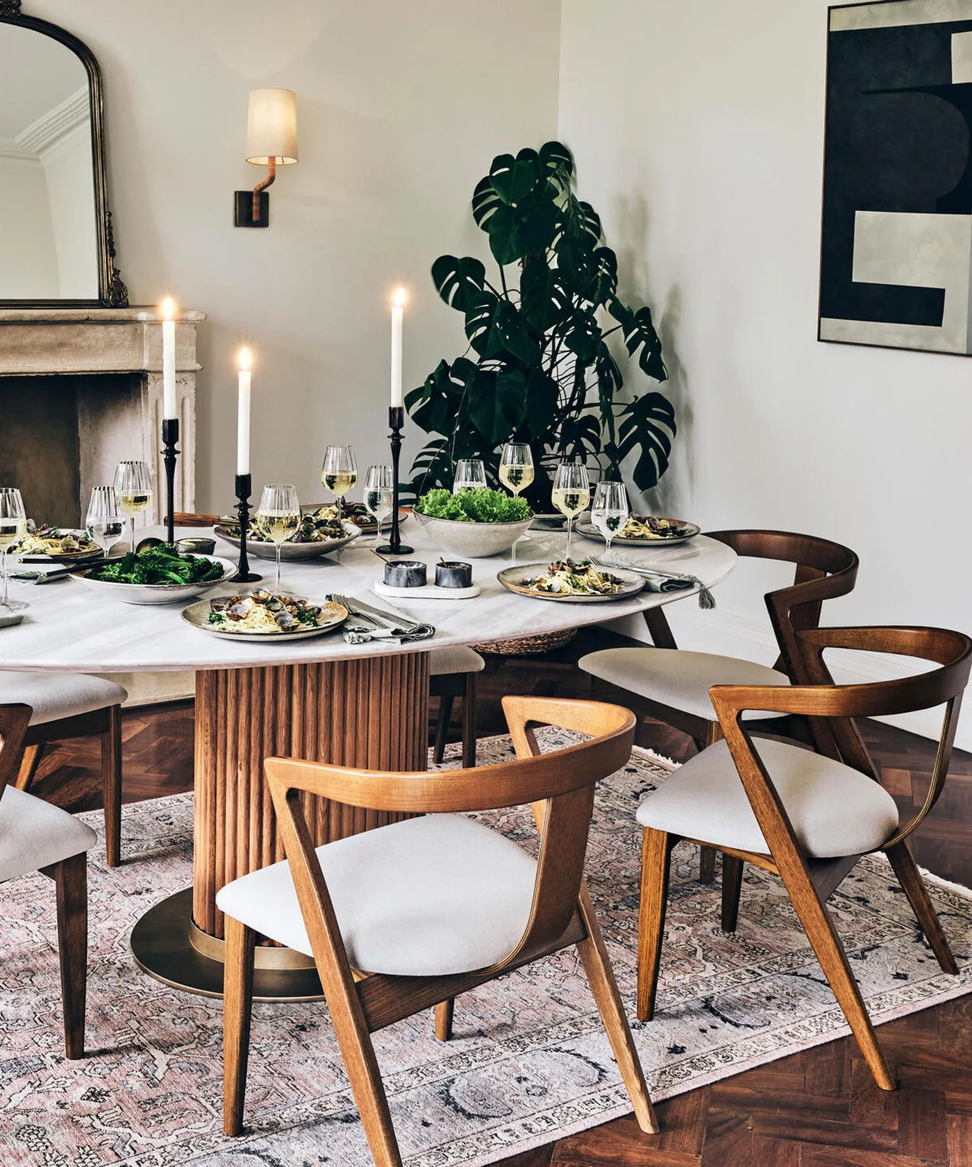 Dining room with a pale round tabletop, fluted wood-colored pedestal, curved open wood chairs, pale seat pads and patterned rug