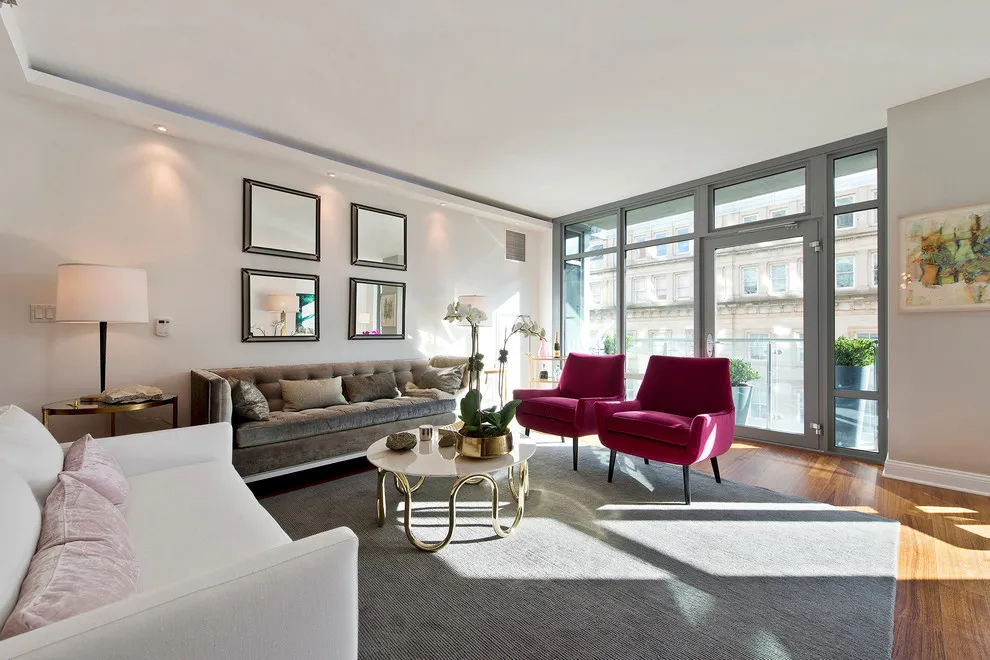 Two burgundy chairs stand near a gray sofa and broad windows opposite a white sofa
