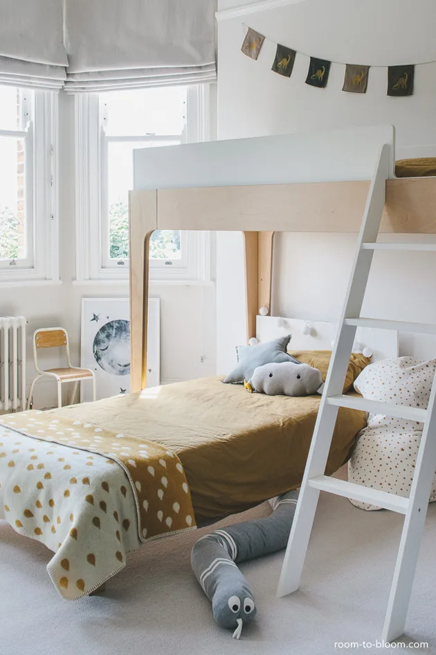 Pale bunk-bed room with mustard bedding, a cloud cushion and a moon print leaning beside the window.