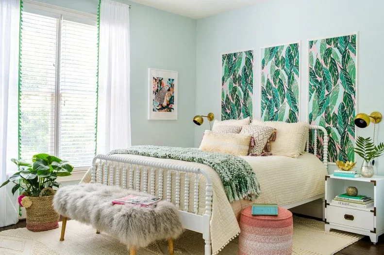 Three tall leafy wall panels hang above a pale spindle bed with cream bedding beside green-trimmed curtains and a small white chest