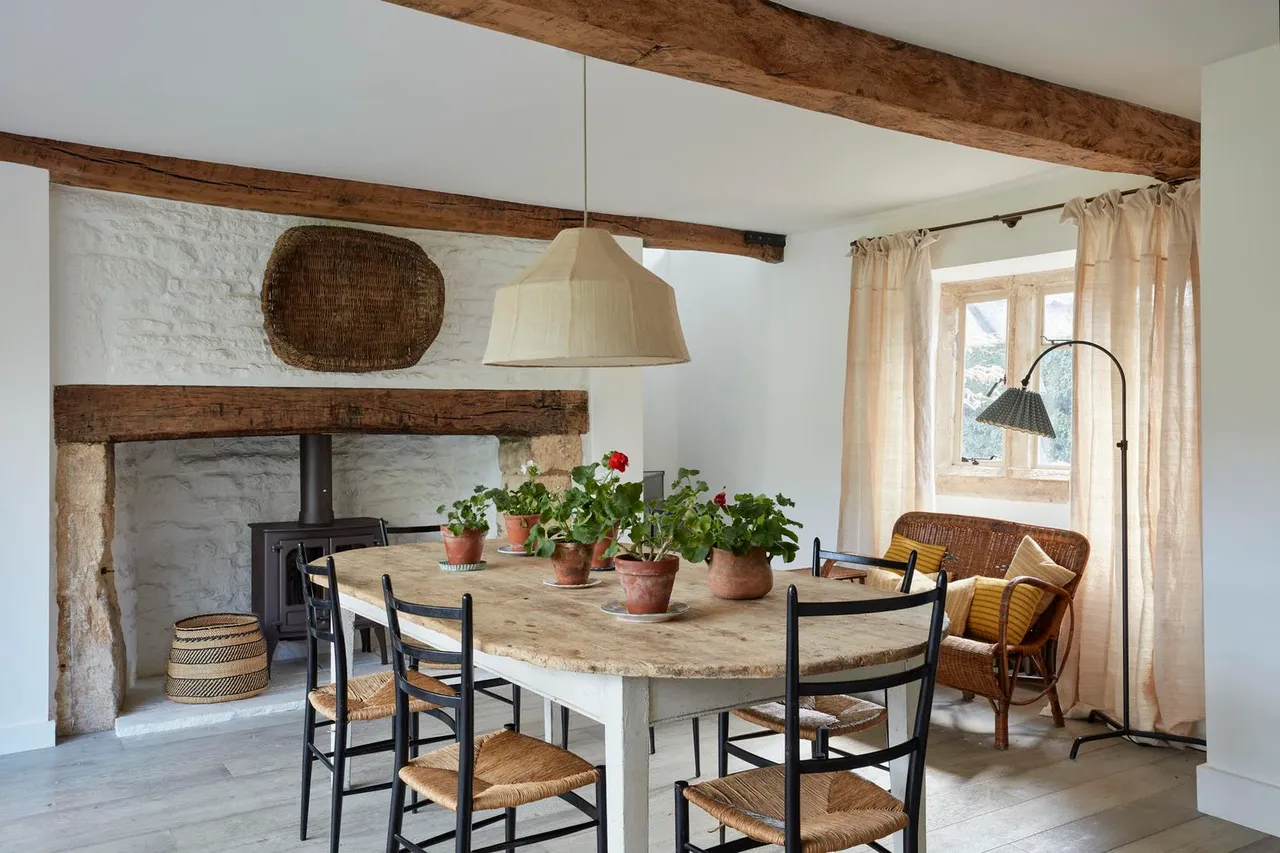 Timber dining furniture sits beside a rustic mantel beneath exposed ceiling beams.