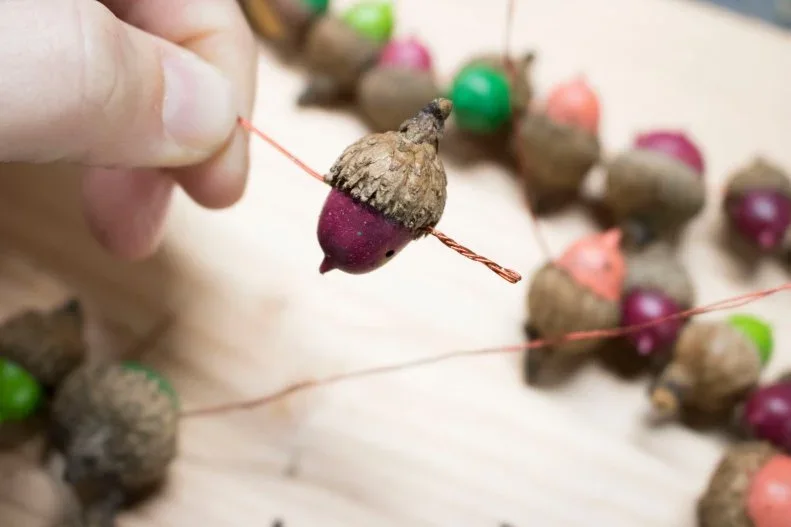 Small acorn-shaped decorations with colored lower halves and textured caps are threaded along a fine cord
