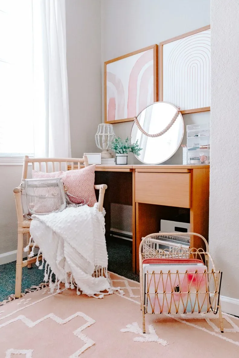 Student desk with wooden chair, white throw, pink cushions, pale pink patterned rug and a freestanding file holder beside the desk.