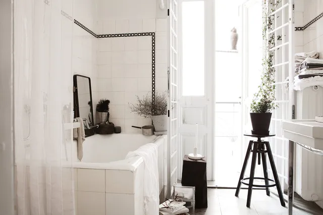 Tall dark stool holding a plant beside a window opposite a white tiled bath
