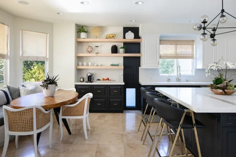 Three wood-toned floating shelves above black cabinetry beside a breakfast table with woven chairs and a bench