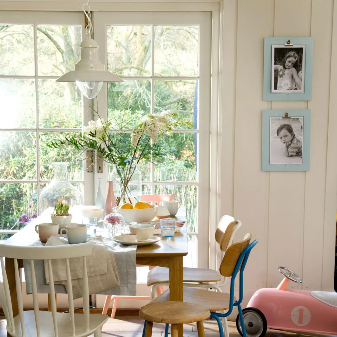 White pendant above a compact wood table with pale, yellow and blue seating beside French doors
