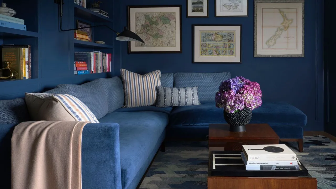 A blue sofa sits against deeper blue walls beneath pale framed artwork.