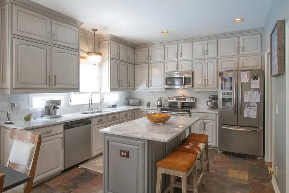 Gray paneled cabinetry surrounds an island with a pale counter and wood stools