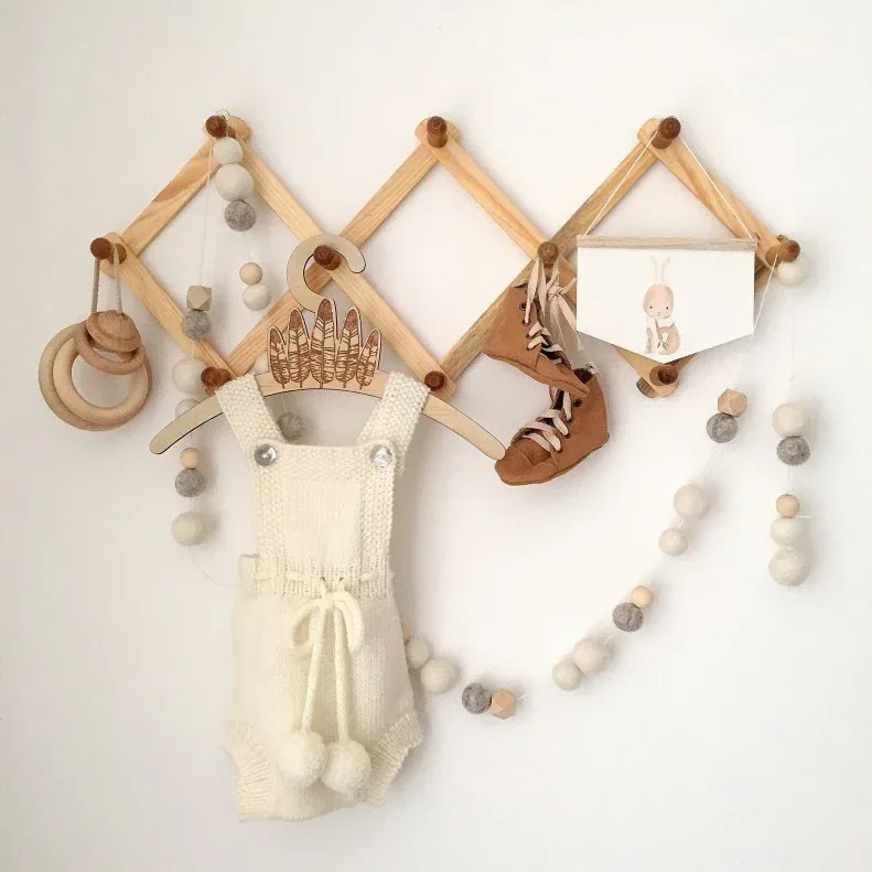 Expandable warm wooden peg rack displaying selected garments and small decorations against pale wall.