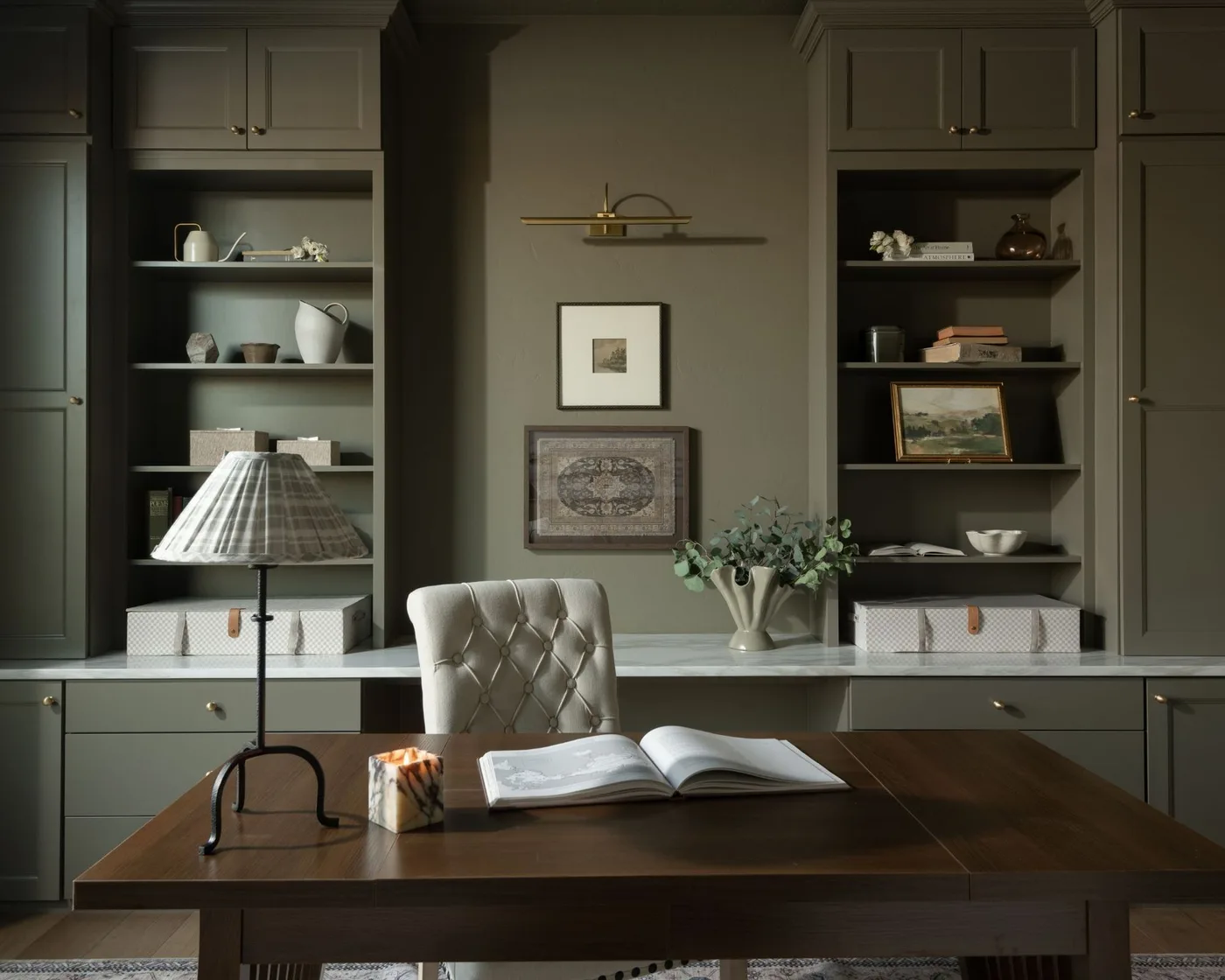 Gray-green office shelving and cabinets with small warm metal pulls and a gold-toned picture light.