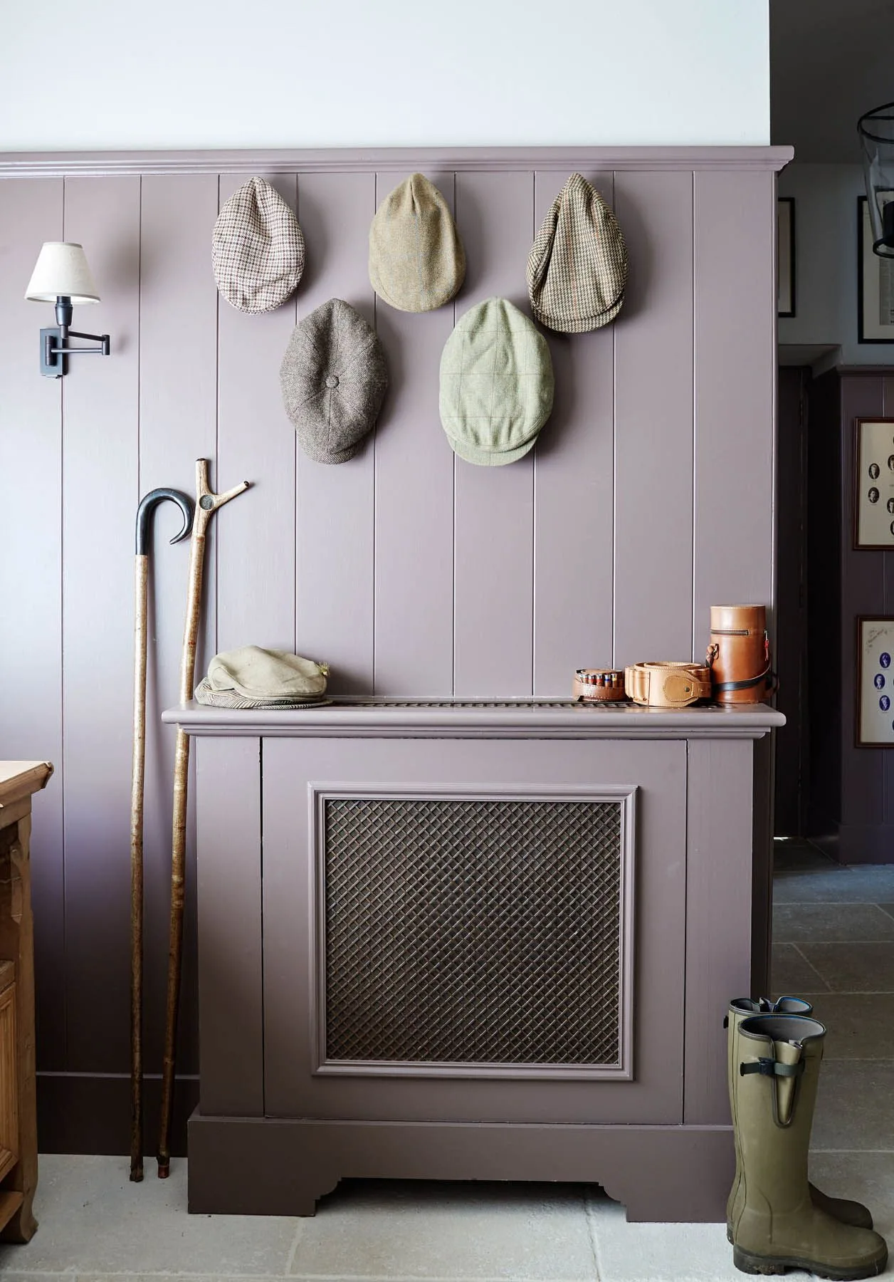 Muted purple paneled wall with five caps on hooks, walking sticks, a vented-front cover and tall boots
