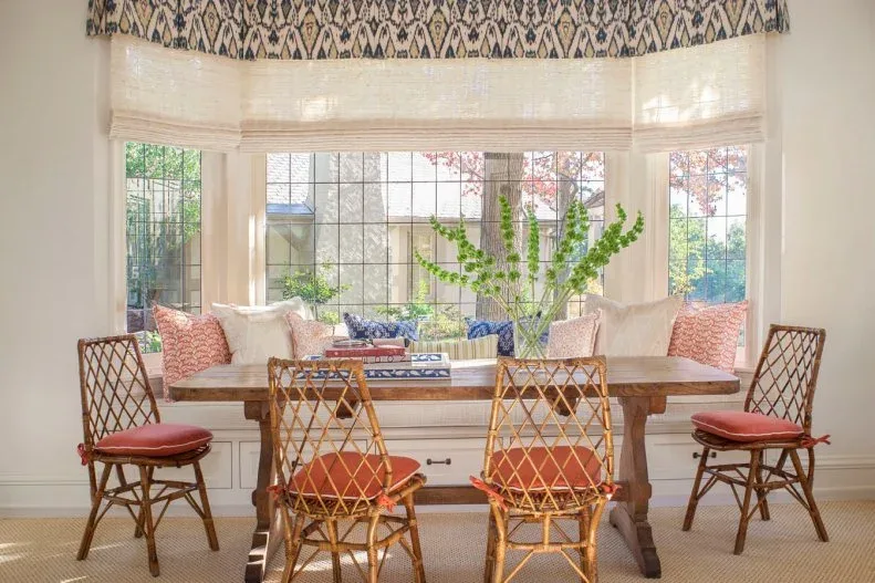 Pale gathered shades beneath a patterned top border around a dining bay with a cushioned bench