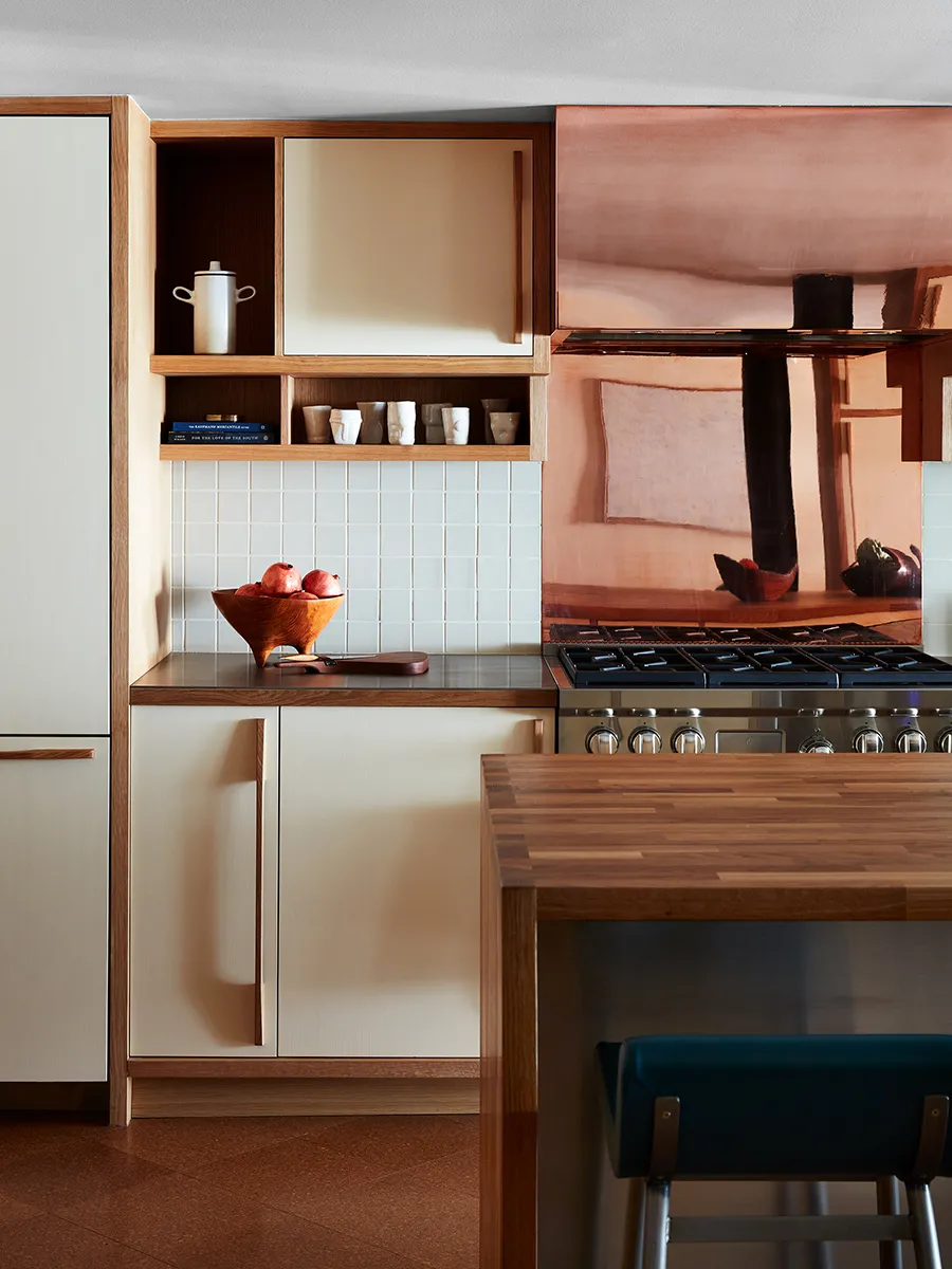 Flat cream cabinet doors sit within wooden frames beside a copper-colored backsplash and open cubbies