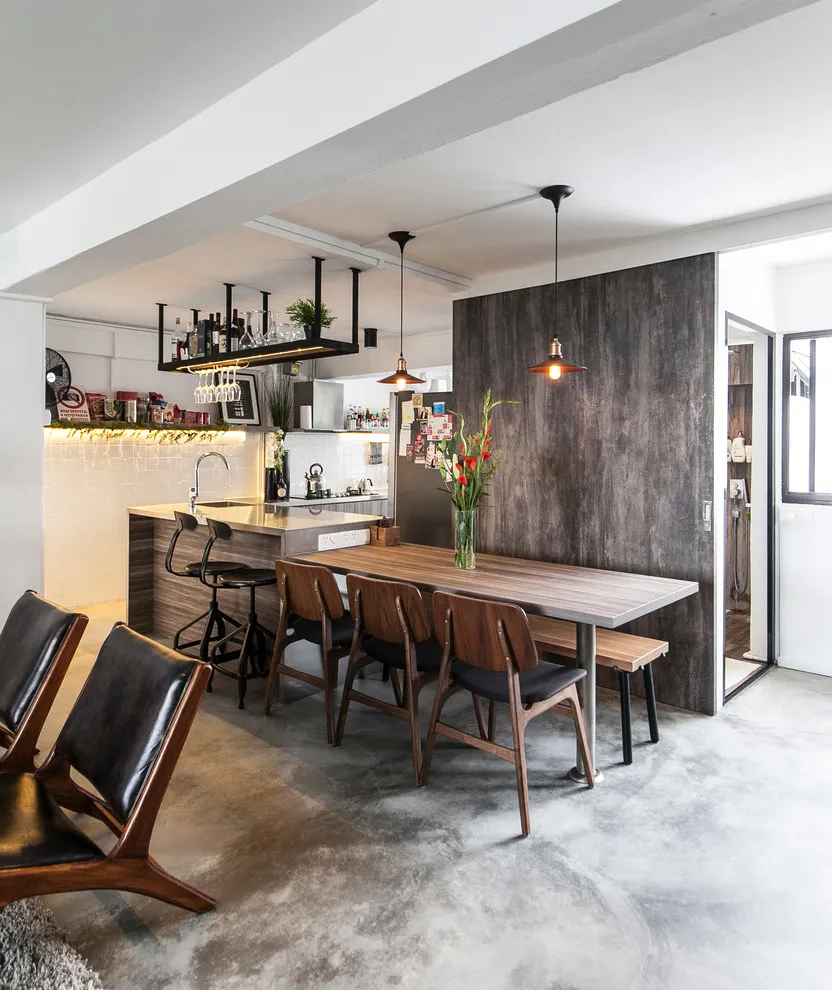 A timber table sits beside an apartment kitchen and a dark partition