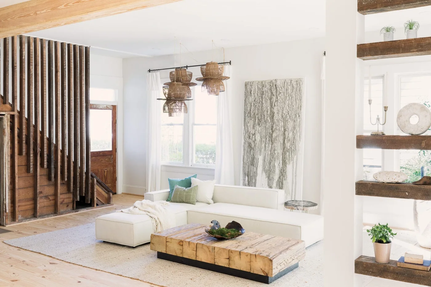A pale sectional sofa and broad wood coffee table sit near vertical wood slats, a white wall, woven pendant shades and open wood shelving