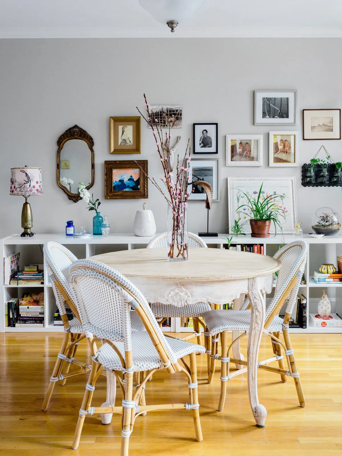 A white round table and pale woven chairs sit below a varied gallery wall.