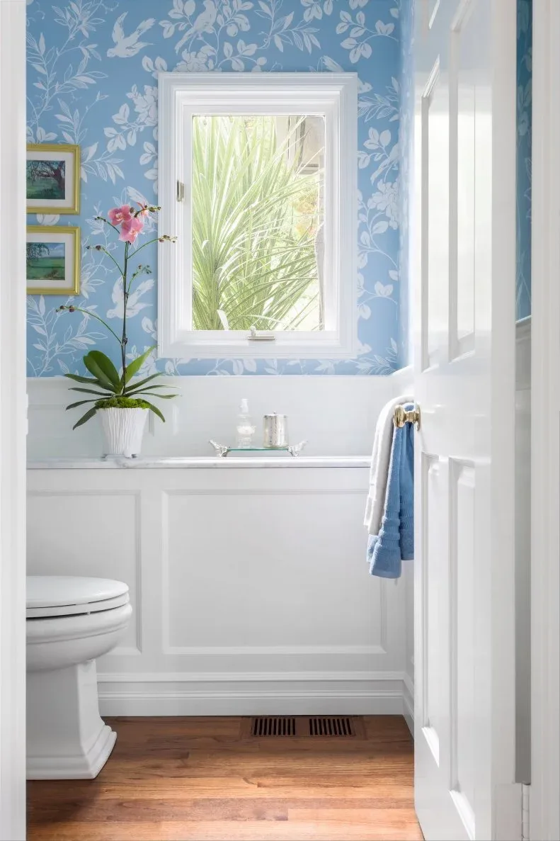 Small powder room with blue botanical wallpaper, white paneled lower walls and narrow window