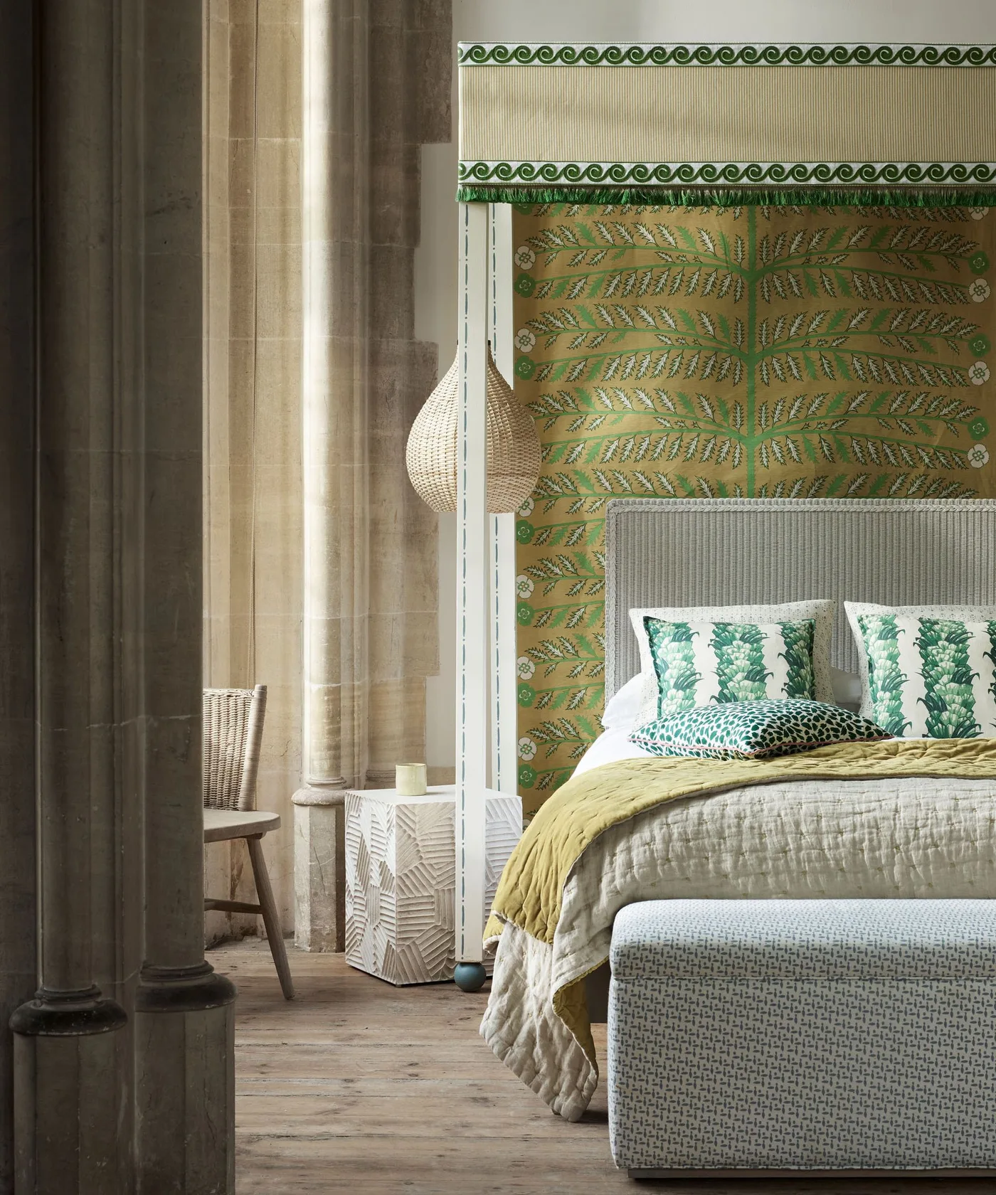 Bedroom with green-and-gold leafy wall panel, pale headboard, green patterned pillows, mustard cover and pale fabric surrounding the bed area.