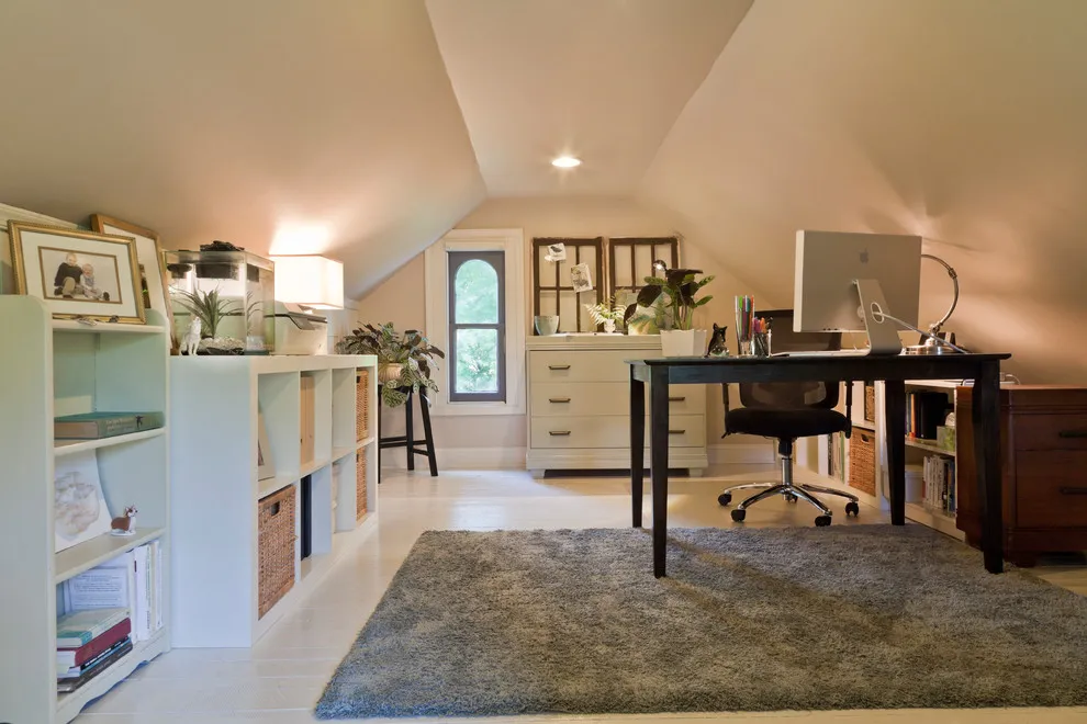 A dark desk and chair sit opposite low pale storage in an attic office