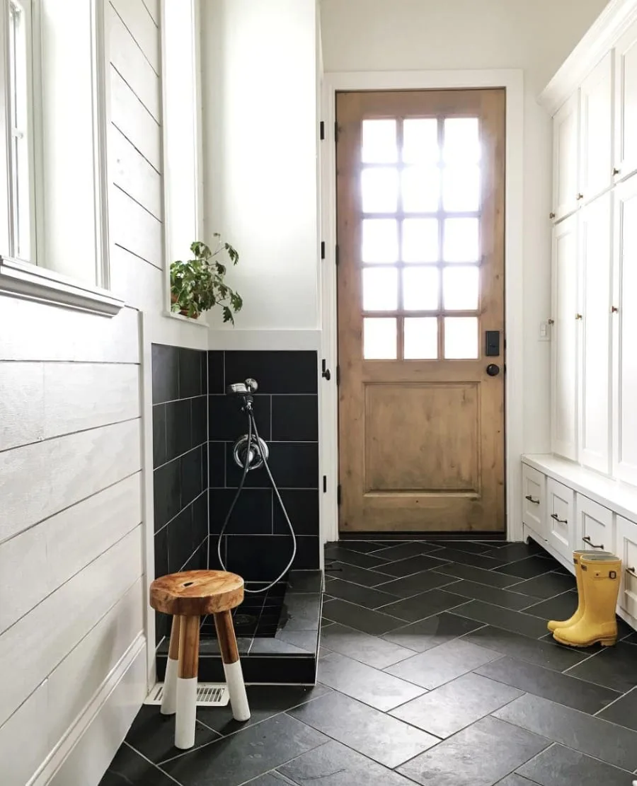 Mudroom with a dark tiled pet-washing recess, wooden glazed door and a white storage bench.