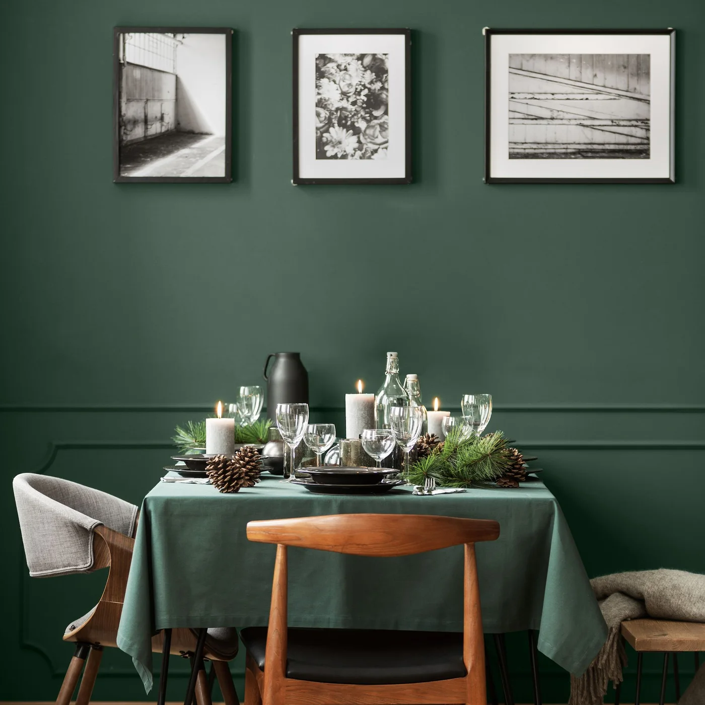 Deep green walls with three framed pale pictures surround a small table covered in green cloth beside wooden seating