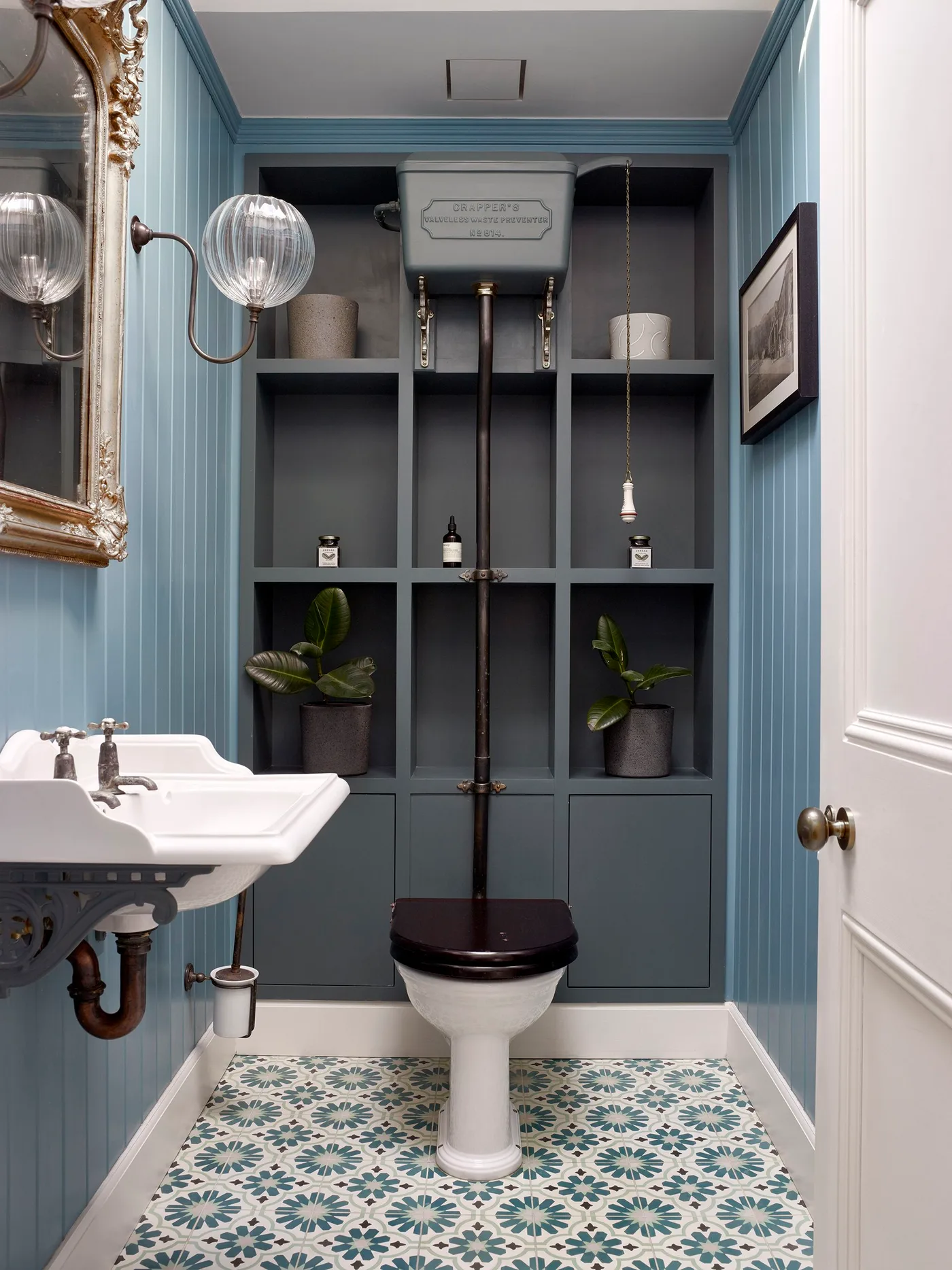 Blue paneled powder room with high toilet cistern, gray cubby shelving and patterned floor