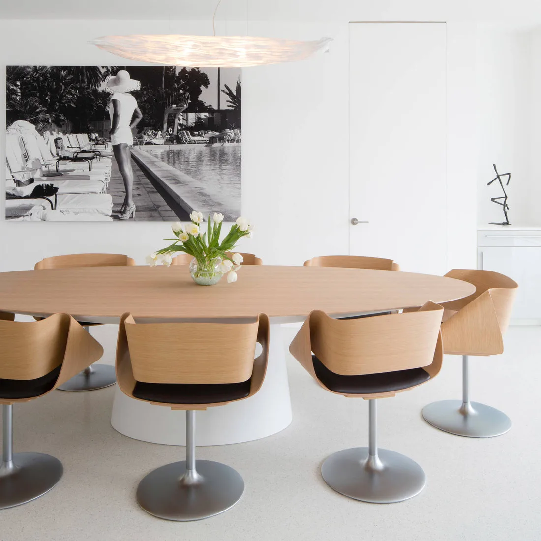 Light wood oval table with curved wood chairs on circular metal bases in a white dining room