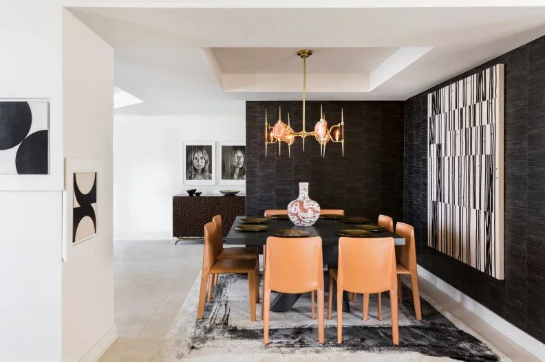 Peach dining chairs around a dark table beside a black-and-white vertically patterned wall and colorful artwork.