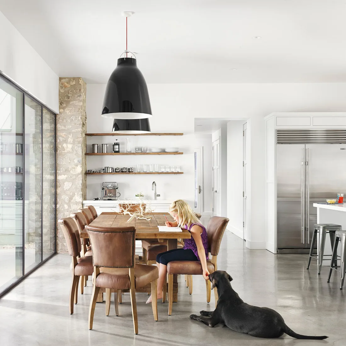 Three wood shelves with glassware beside a kitchen dining table and brown upholstered chairs